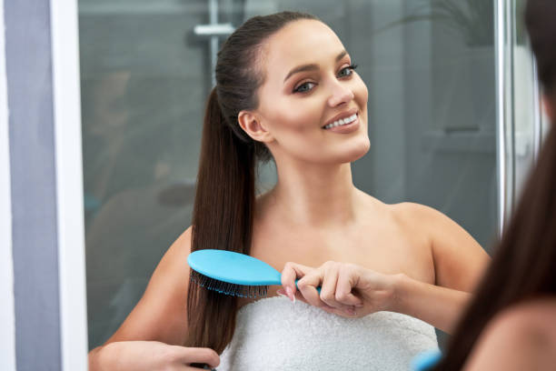 Woman brushing hair in bathroom after shower Picture of beautiful woman looking on reflection in the mirror after shower brushing hair stock pictures, royalty-free photos & images