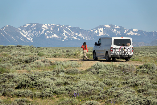 Looking from the Arapahoe National Wildlife Refuge in North Park, Colorado, a woman walks past her camper van and mounted mountain bicycle with the snow covered Park Range and Mount Zirkel Wilderness in the background.