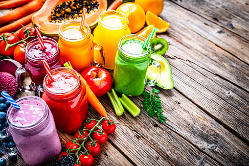 Healthy eating: high angle view of fresh rainbow colored fruits and vegetables smoothies in Mason jars arranged side by side on rustic wooden table. Fruits and vegetables included in the composition are papaya,  tomatoes, cucumber, oranges, strawberries, beetroot, avocado and carrots. The composition is at the left of an horizontal frame leaving useful copy space for text and/or logo at the right. High resolution 42Mp studio digital capture taken with SONY A7rII and Zeiss Batis 40mm F2.0 CF lens