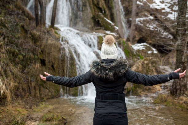istock Woman standing by waterfall with her hands raised 1304937694