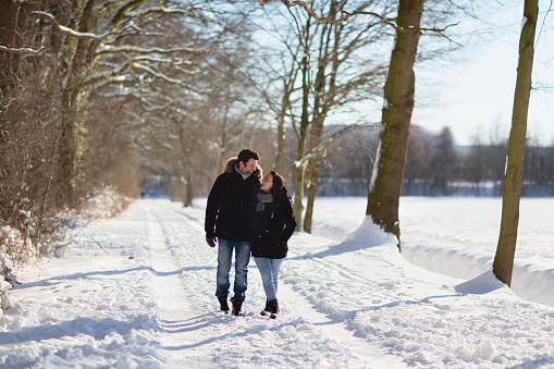 Midadult couple walking on a treelined  avenue at a sunny day in february, a foreste at the left side, an open field at the right side, they are looking at each other