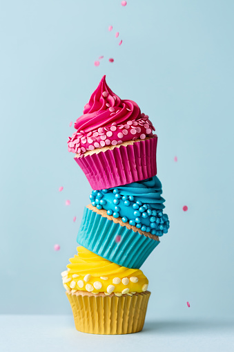 Stack of three colorful cupcakes with falling sprinkles