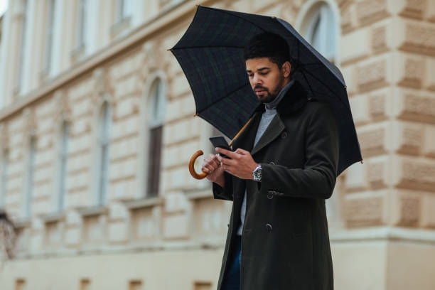 istock Young man using mobile phone outdoors on a rainy day 1304942623