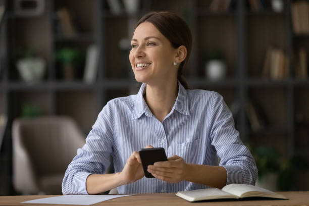istock Smiling woman sit at desk use modern smartphone 1304943779