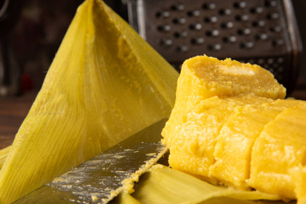 istock Pamonha, Brazilian corn food, called pamonha. On a rustic table with knife and old corn grater, low key portrait, dark abstract background, selective focus. 1304946283