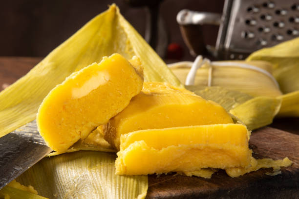 istock Pamonha, Brazilian corn food, called pamonha. On a rustic table with knife and old corn grater, low key portrait, dark abstract background, selective focus. 1304946300