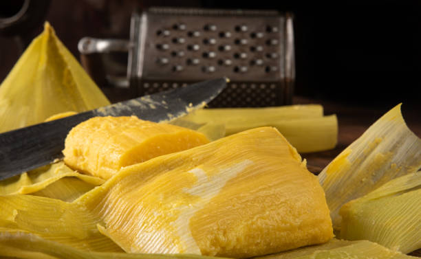 istock Pamonha, Brazilian corn food, called pamonha. On a rustic table with knife and old corn grater, low key portrait, dark abstract background, selective focus. 1304946306