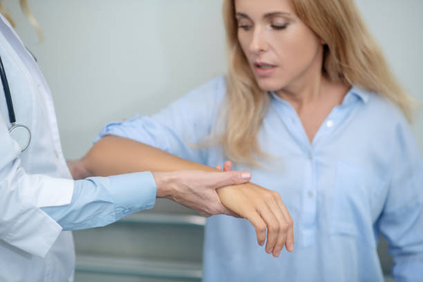 Unhappy woman with raised arm being examined by doctor Pain syndrome. Unhappy blonde woman with painful raised arm being examined by doctor in white coat at medical facility forearm stock pictures, royalty-free photos & images