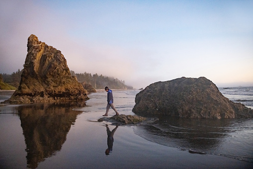 Tourist and a surfer in the mist at sunrise at Cox Bay Beach, Tofino, Vancouver Island, British Columbia, Canada.