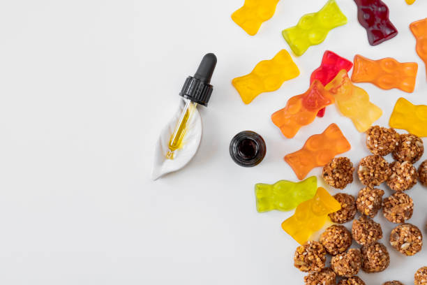 Gummy bears, cannabis cookies and cbd oil dropper in white backdrop. THD or cbd sweets in form of gelatine gummi bears and essential oil pipette background: calming edible food supplements cannabis gummy bears stock pictures, royalty-free photos & images