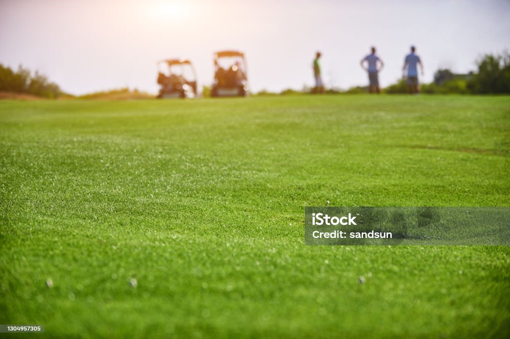 people playing golf on a summer day. Golf hole in the foreground, blurred people in the background people playing golf on a summer day. Golf hole in the foreground, blurred figures in the background. Golf Stock Photo
