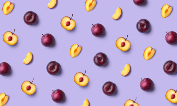 紫色の背景に新鮮な全体とスライス梅のカラフルなフルーツパターン - プラム ストックフォトと画像
