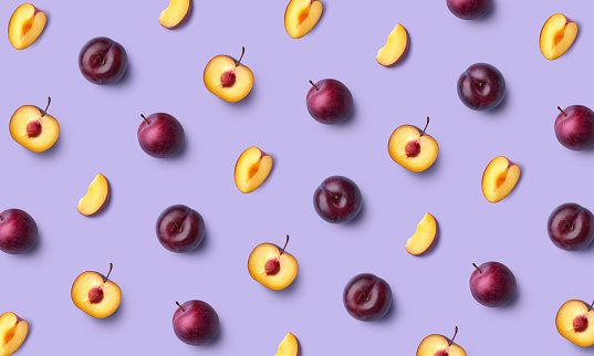 Colorful fruit pattern of fresh whole and sliced plum on purple background