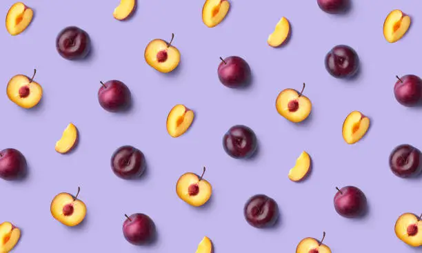 Colorful fruit pattern of fresh whole and sliced plum on purple background, flat lay, top view