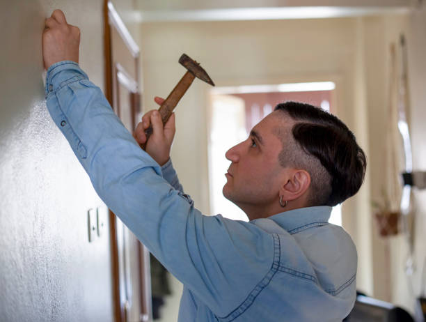 istock Young man hammering nail on white wall 1304960230