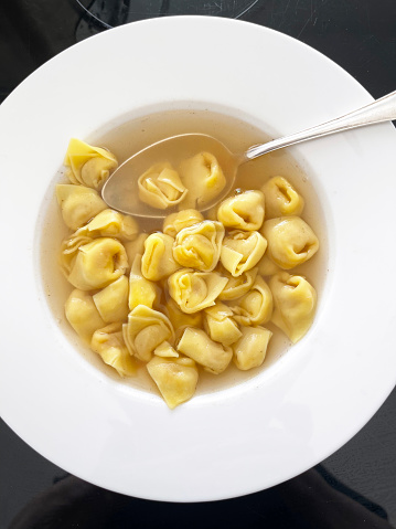 close-up of tortellini in broth on white plate