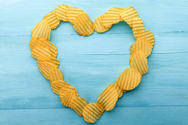 istock Potato chips heart shape on a blue wooden background 1304964829