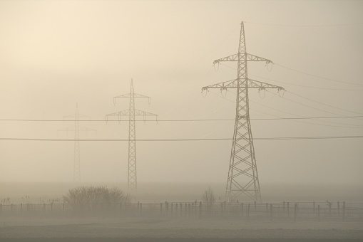 The sun shines through the fog and reveals the electricity pylon
