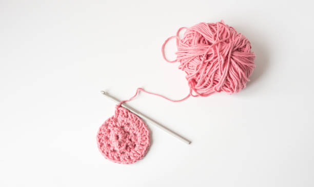 Crochet hook and pink yarn on white background from above