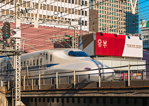 tokyo, japan - march 02 2021: Close up on a Shinkansen bullet train 700 series passing at Yurakucho station in front advertising signs of Tokyo 2020 Olympic Games on the roof of Tokyo Sports Square.