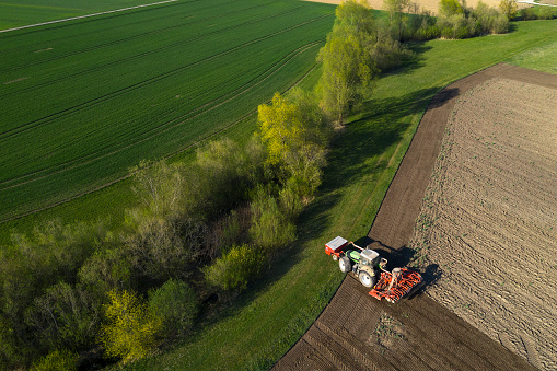 Aerial spring landscape with fresh green trees and a tractor working in field.