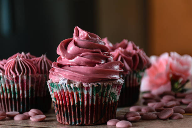 istock Closeup of three chocolate cupcakes with pink butter cream. Next to Ruby chocolate callets. Brown and orange background. 1304989830