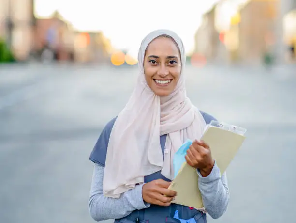 A beautiful Muslim female nurse wearing a hijab is smiling at the camera.