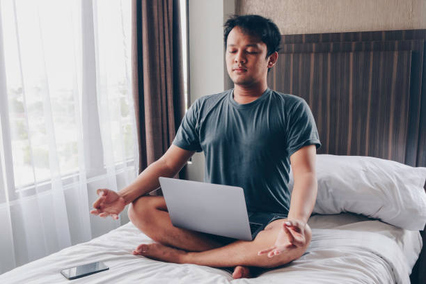 istock Work from home. Young asian man sits on a bed. Home workplace. Break, relaxation at the time of work. 1305001204