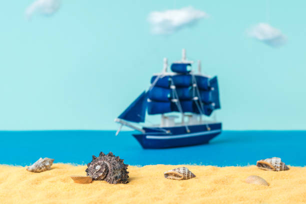 istock Installation of seashells on a sandy beach with a sailing ship floating away. 1305012401