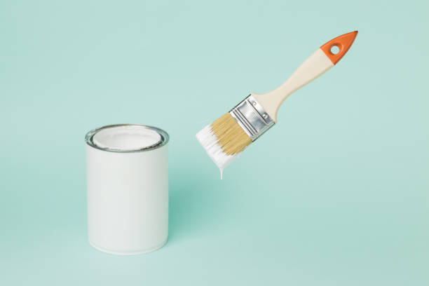 istock A jar of white paint and a levitating brush on a blue background. 1305012405