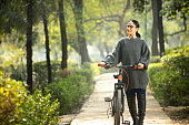 Woman walking and pushing bicycle at park