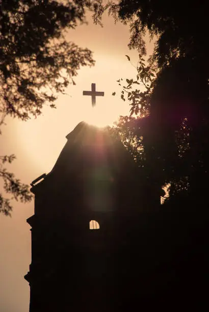 Telephoto shot of a belfry of a Catholic church in Tepoztlan, Mexico.  Photo shows the surrounding foliage that frames the main subject under a clear sky during the golden hour of a sunset.
