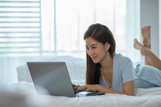 istock Beautiful Attractive Asian young woman lying on bed and using computer laptop for using social media and shopping online relax in cozy bedroom in holiday,Lifestyle in home Concept 1305015827