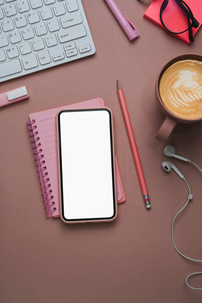 istock Female workplace with mobile phone notebook, coffee cup and office supplies on pink background. 1305024743