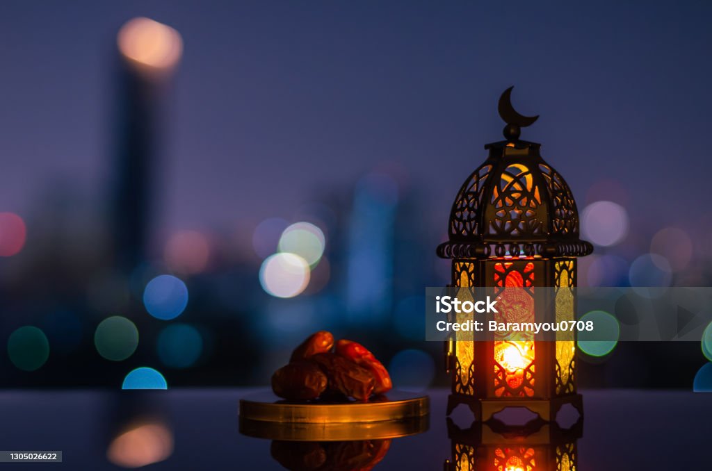 Ramadan Kareem lantern and dates fruit with city light background. Lantern that have moon symbol on top and small plate of dates fruit with night sky and city bokeh light background for the Muslim feast of the holy month of Ramadan Kareem. Ramadan Stock Photo