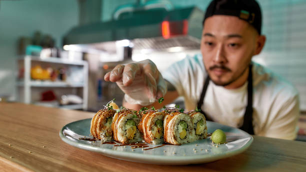 istock Professional sushi chef wearing protective gloves decorating rolls served on plate at commercial kitchen 1305026917