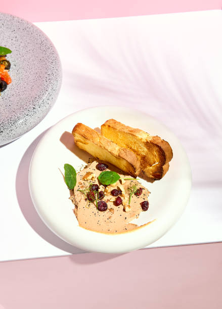 istock Pate with Bread on white plate. Restaurant appetizer plate on white table with pink wall. Day sunlight with hard shadow of fern palm leaves. Summer or spring restaurant food concept. 1305028556