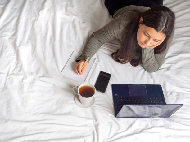 istock Woman lying in bed bored looking in a laptop while working from home. 1305031542