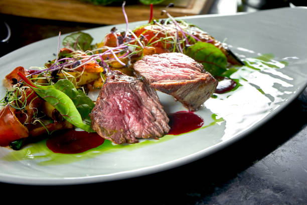 istock Medium rare beef medallions with vegetable garnish, served on a white plate. Dark marble background. Barbecue meat, restaurant food. Tasty steak 1305031574