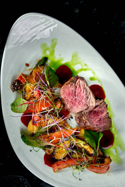 istock Medium rare beef medallions with vegetable garnish, served on a white plate. Dark marble background. Barbecue meat, restaurant food. Tasty steak 1305031618