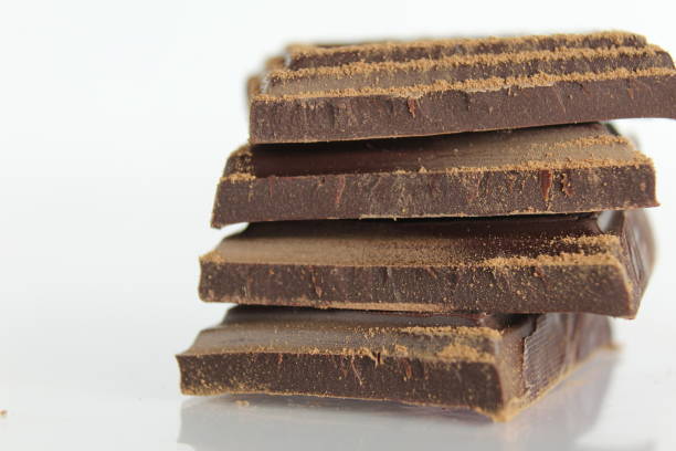 istock Dark bitter chocolate pieces stacked slide lies on a white background with a reflection with a place for text and copyspace 1305035755