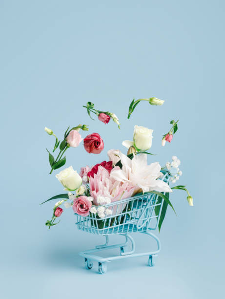 Shopping trolley with flying flowers on pastel blue background
