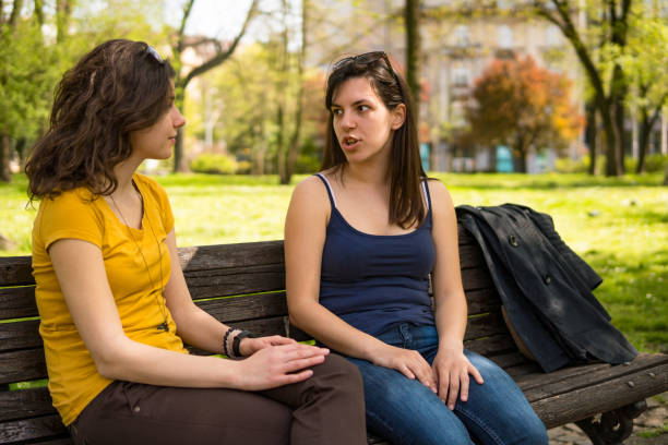 Two girl friends sitting on the park bench and talking, on a sunny April day.