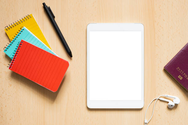 Flat lay with copy space, some office supply, passport and a tablet with white screen are arranged on a wooden table. Concept of showing information on a display, touch screen, smart device.