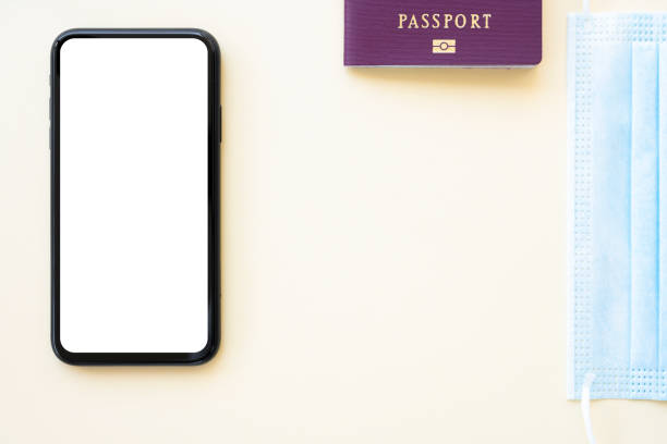istock Flat lay with copy space, a passport, face mask and a smartphone with white screen are arranged on a cream colored background. Concept of showing information on a display during the Covid-19 pandemic. 1305038393