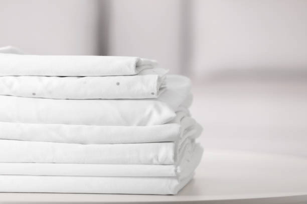 New clean folded bed linens on table indoors. Space for text