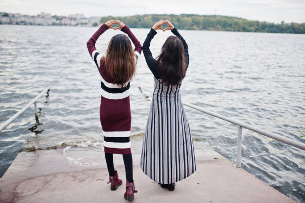 Portrait of back two young beautiful indian or south asian teenage girls in dress show heart by hands.