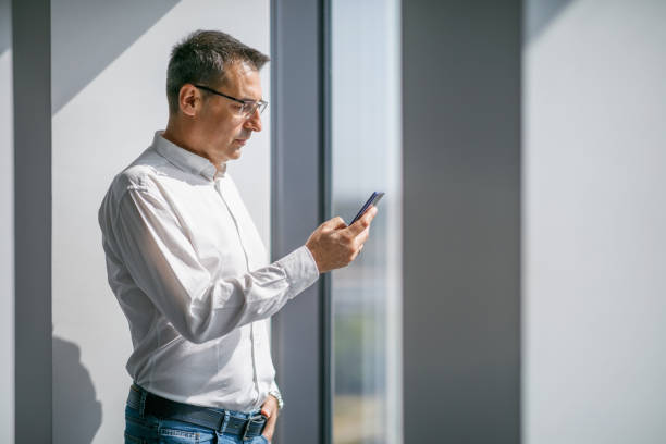istock Businessman standing in sunlight and reading text message 1305046853