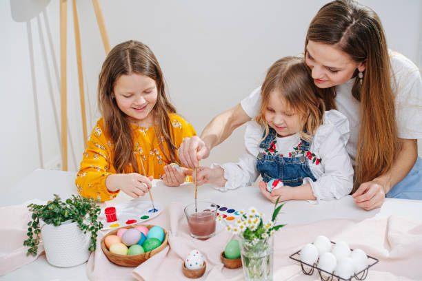 istock Loving mother observing her two daughters as they paint easter eggs 1305048043