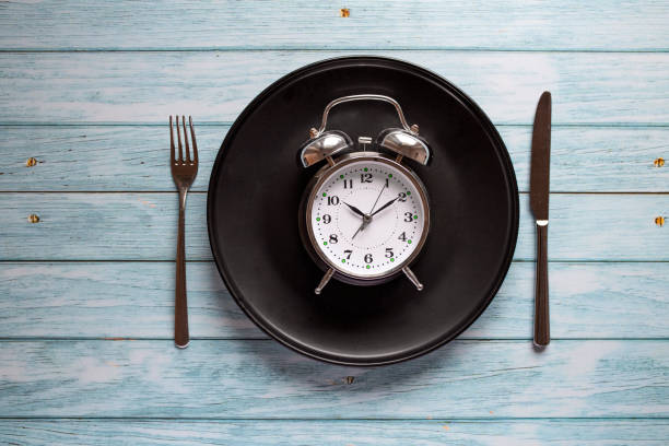 istock Meal planning for diet concept, Intermittent fasting concept with clock on plate, fork and knife on wooden table, Clock on plate with fork and knife, intermittent fasting, meal plan, weight loss 1305050695